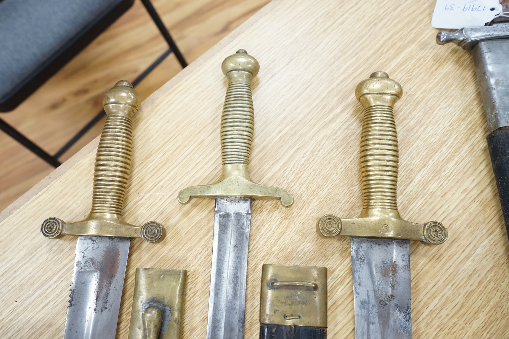Three Continental infantry officer’s sidearms briquette, the first stamped Paris, in its brass mounted leather scabbard, another similar with sawback blade (illegible stamp), and another similar with thin blade, stamped